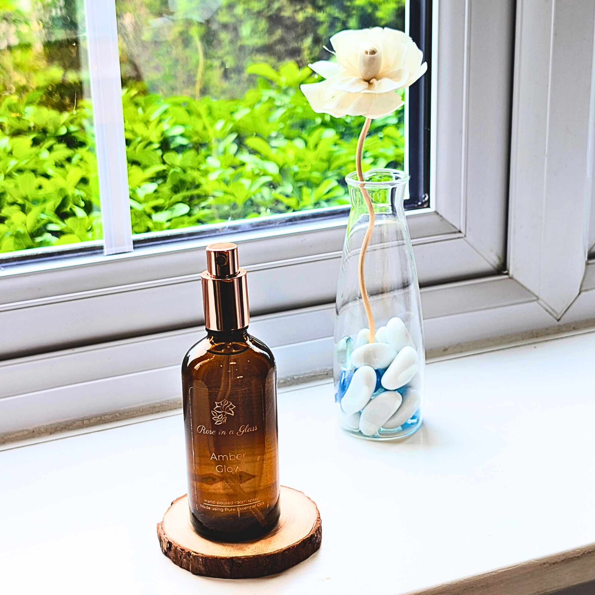 Amber Glow Aromatherapy room spray on a windowsill with a rose diffuser for a tranquil home environment