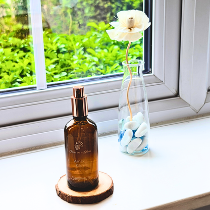 Amber Glow Aromatherapy room spray on a windowsill with a rose diffuser for a tranquil home environment